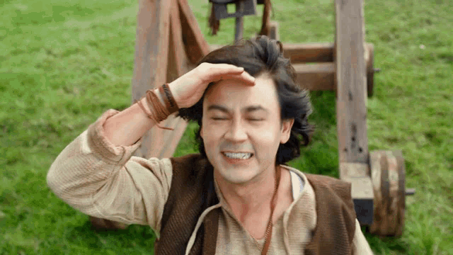 a man with his hand on his forehead is smiling in a field .