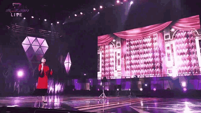 a woman in a red dress is singing into a microphone on a stage with a live sign above her