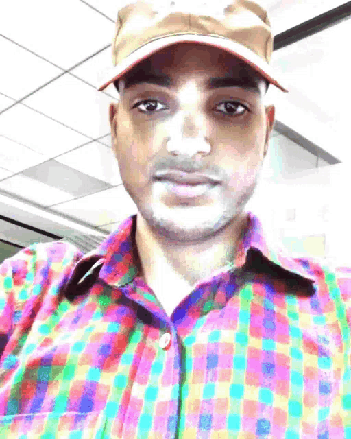a man wearing a hat and a colorful plaid shirt looks at the camera