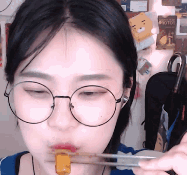 a girl wearing glasses is eating a piece of food with chopsticks
