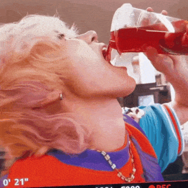 a person is drinking a red liquid from a plastic cup .