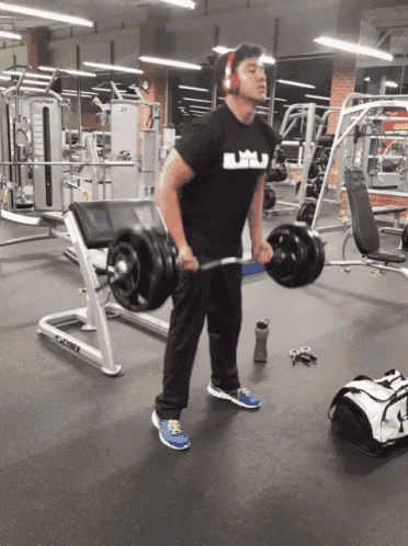 a man wearing headphones is lifting a barbell in a gym with a cybex machine