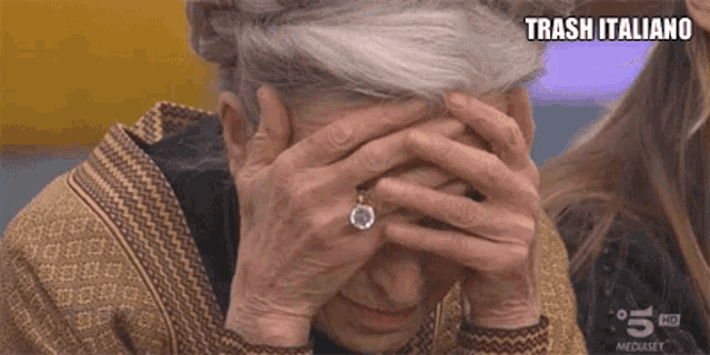 an older woman is covering her face with her hands and a ring on her finger .