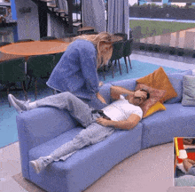 a man is laying on a blue couch while a woman stands next to him