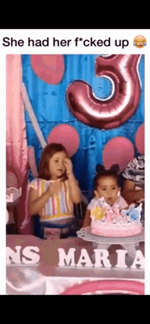 two little girls are sitting at a table with a birthday cake and balloons behind them ..