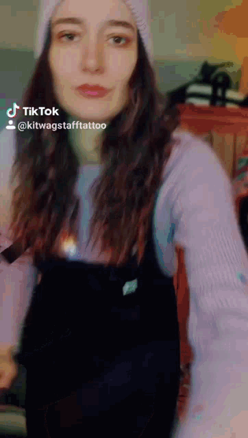 a woman wearing a beanie and overalls has a tiktok sticker on her face
