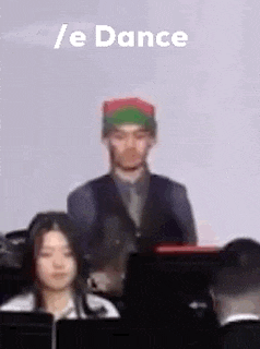 a man in a green and red hat is standing in front of a group of people in a room .