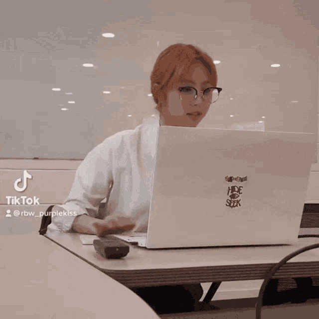 a woman sitting at a table with a laptop that has a sticker that says hide seek