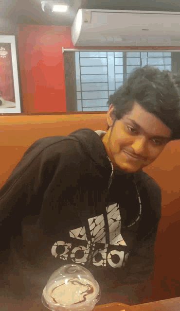 a young man wearing a black adidas sweatshirt stands next to a cup of food