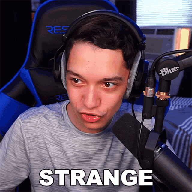 a young man wearing headphones and a blue microphone says " strange "