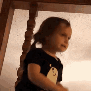 a little girl is standing on a wooden staircase and making a funny face .