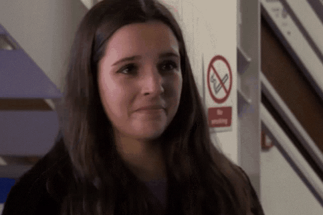a girl is standing in front of a no smoking sign