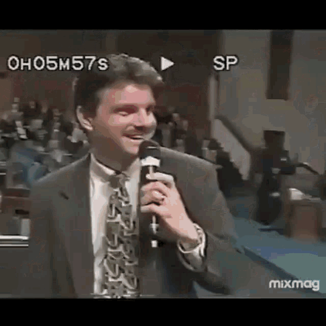 a man in a suit and tie is holding a microphone and smiling in front of a crowd .