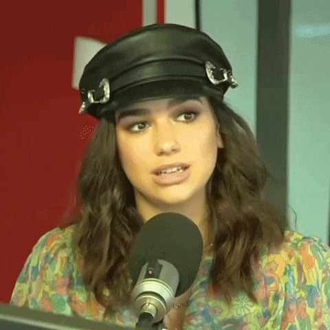 a woman wearing a hat and a floral shirt is talking into a microphone .