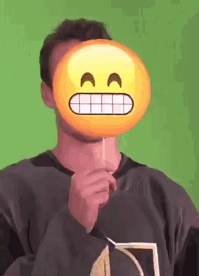 a man is holding a lollipop with an emoji face on it in front of his face