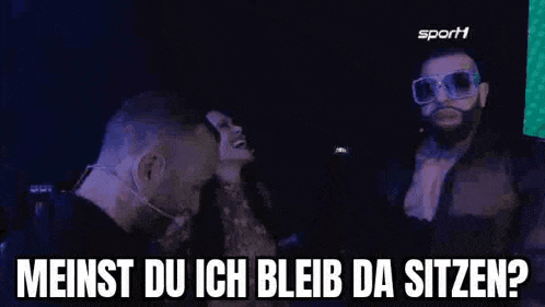 a man and a woman are talking to each other in a dark room and the man is wearing sunglasses .