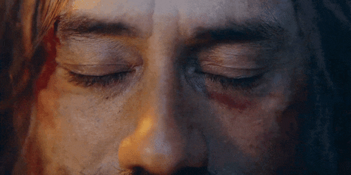 a close up of a man 's face with blood on his face and his eyes closed .