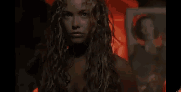 a woman with long curly hair is standing in a dark room with a red background .