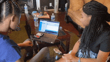 a woman sits at a table with a laptop and water bottles