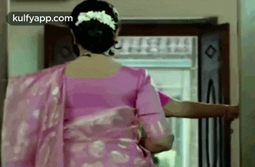 a woman in a pink saree is walking into a doorway .