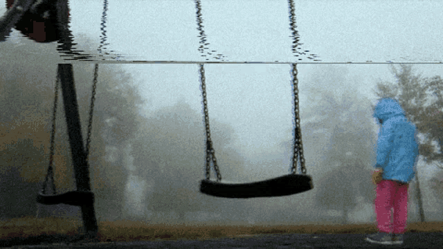 a girl in a blue jacket stands next to a swing