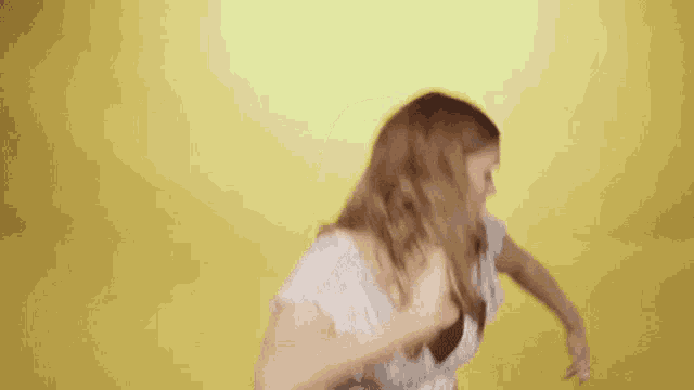 a woman in a crop top and jeans is dancing with her arms outstretched against a yellow background .
