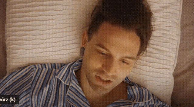 a man in a striped shirt is laying on a bed with a white pillow .