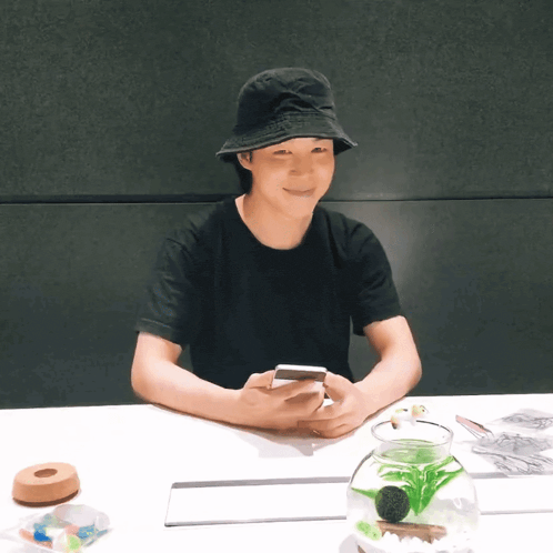 a person wearing a black hat is sitting at a table looking at a cell phone