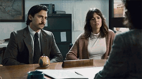 a man and woman are sitting at a desk with an apple on the desk