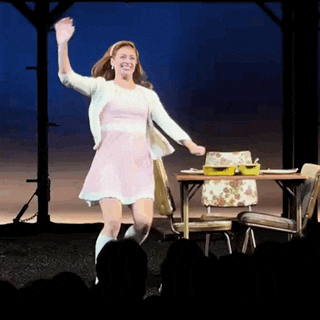 a woman in a pink dress is dancing on stage in front of a table and chairs