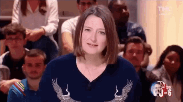 a woman wearing a sweater with an eagle on it is sitting in front of a crowd of people .