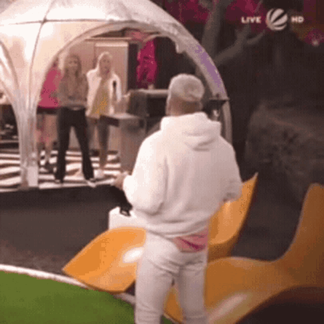 a man in a white hoodie is standing in front of a group of people watching a live tv show