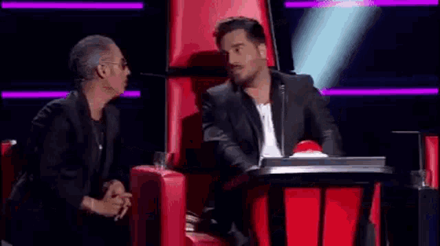 a man in a suit is sitting next to another man in a chair on a stage .