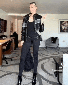 a woman wearing a black leather jacket and black leggings is standing in a living room