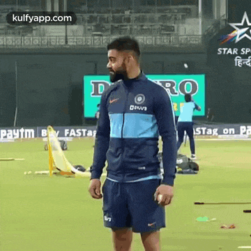 a man in a blue jacket and blue shorts is standing on a cricket field .
