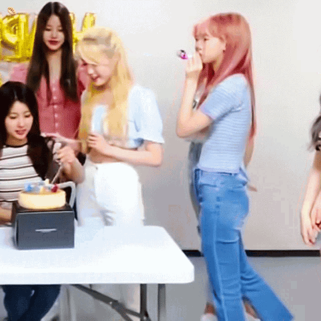 a group of girls are gathered around a table with a cake on it and balloons that say ' u ' on them