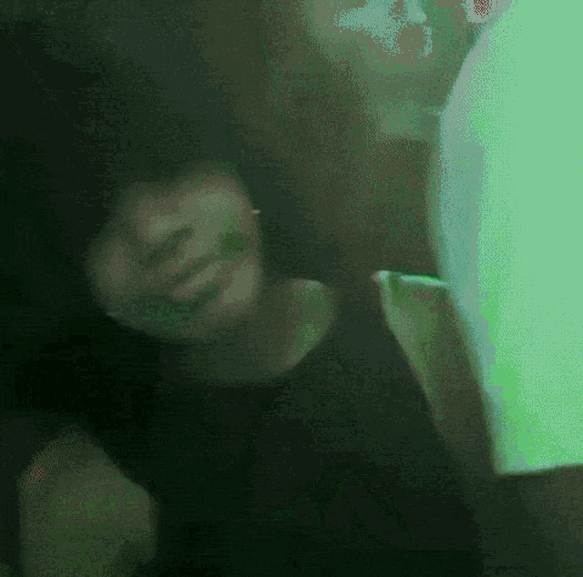 a woman in a black shirt is dancing in a dark room with green lights behind her