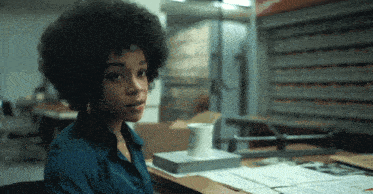 a woman in a blue shirt sits at a desk with a white mug on top of a book