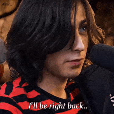 a man with long hair says " i 'll be right back " in front of a microphone