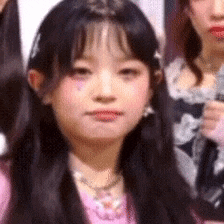 a girl with long black hair is wearing a pink shirt and a pink necklace