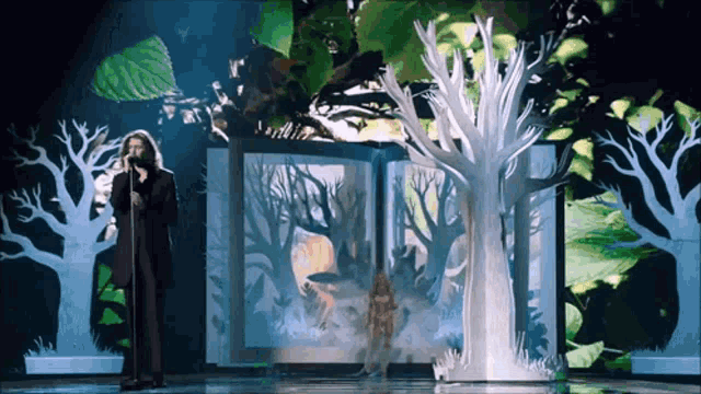 a woman sings into a microphone in front of a book with trees on it