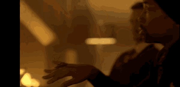 a man with a ring on his finger is talking to another man in a dark room