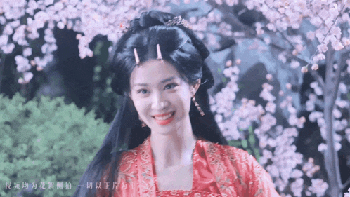 a woman in a red dress smiles in front of a cherry blossom tree