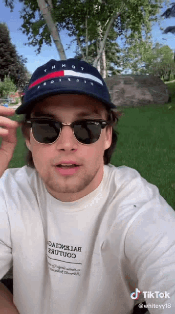 a man wearing sunglasses and a tommy hilfiger hat takes a selfie