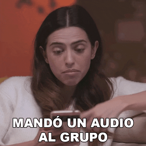 a woman sitting on a couch looking at her phone with the words mando un audio al grupo written above her
