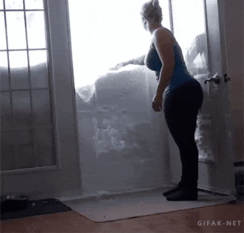 a woman in a blue tank top is standing in front of a door that has snow on it