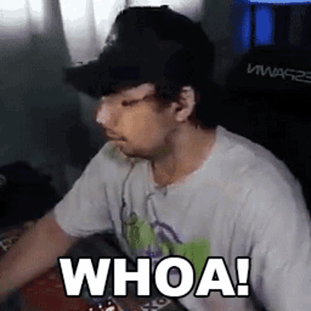 a man wearing a hat and headphones is sitting at a desk with the words whoa ! written on the screen .