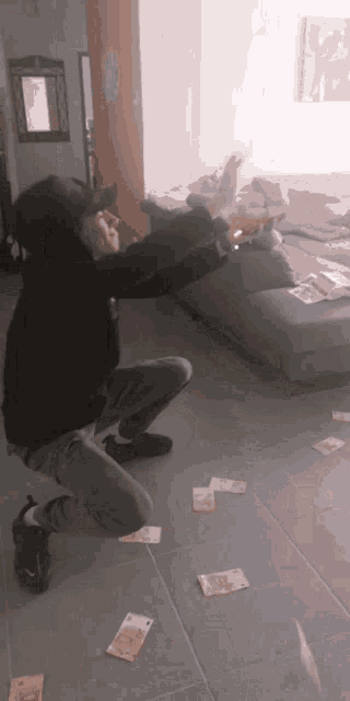 a man is squatting down in a living room with a bunch of money on the floor