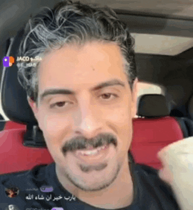 a man with a mustache is smiling while sitting in a car .