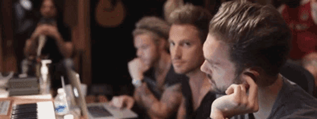 a group of men are sitting at a table looking at laptops .
